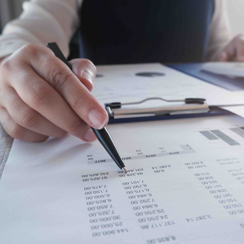 Female working in office, studying using calculator and writing something with documents and chart on table